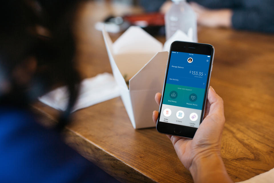 A person holding a smartphone with PayPal's app displayed.