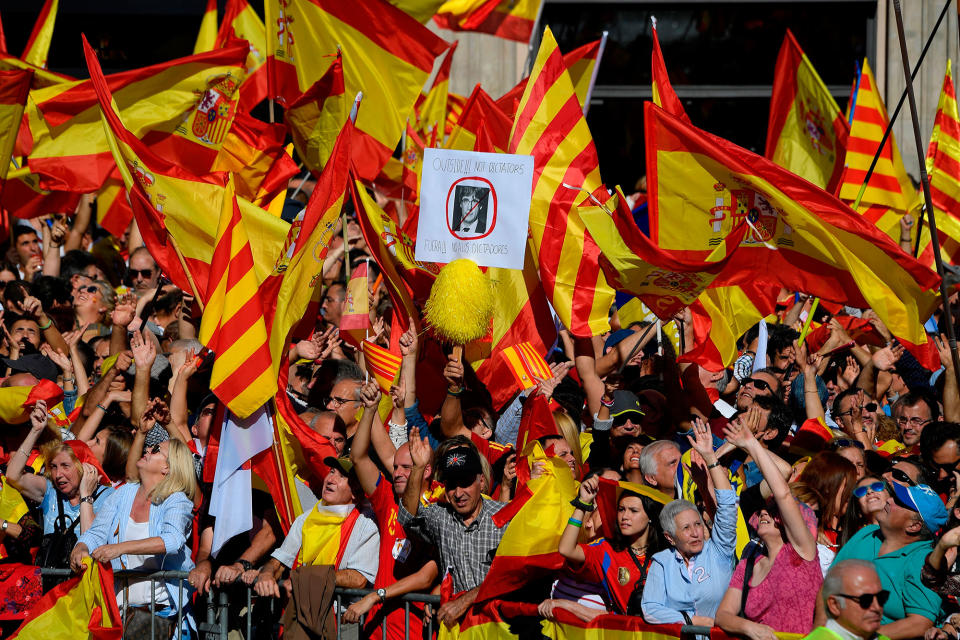 <p>A demonstrator holds a placard bearing a crossed-out portrait of Catalan regional leader Carles Puigdemont, who was officially ousted by Madrid, reading “Dictators out” as others wave Spanish and Catalan Senyera flags during a pro-unity demonstration in Barcelona on Oct. 29, 2017. (Photo: Lluis Gene/AFP/Getty Images) </p>