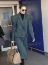 <p>In a teal-gray trench coat, black turtleneck, black shades, and beige bag.</p>