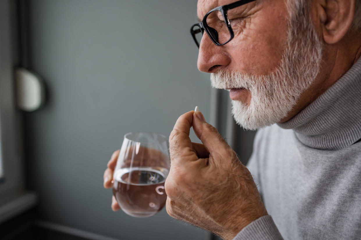 A man holds a pill in one hand and a glass of water in the other.