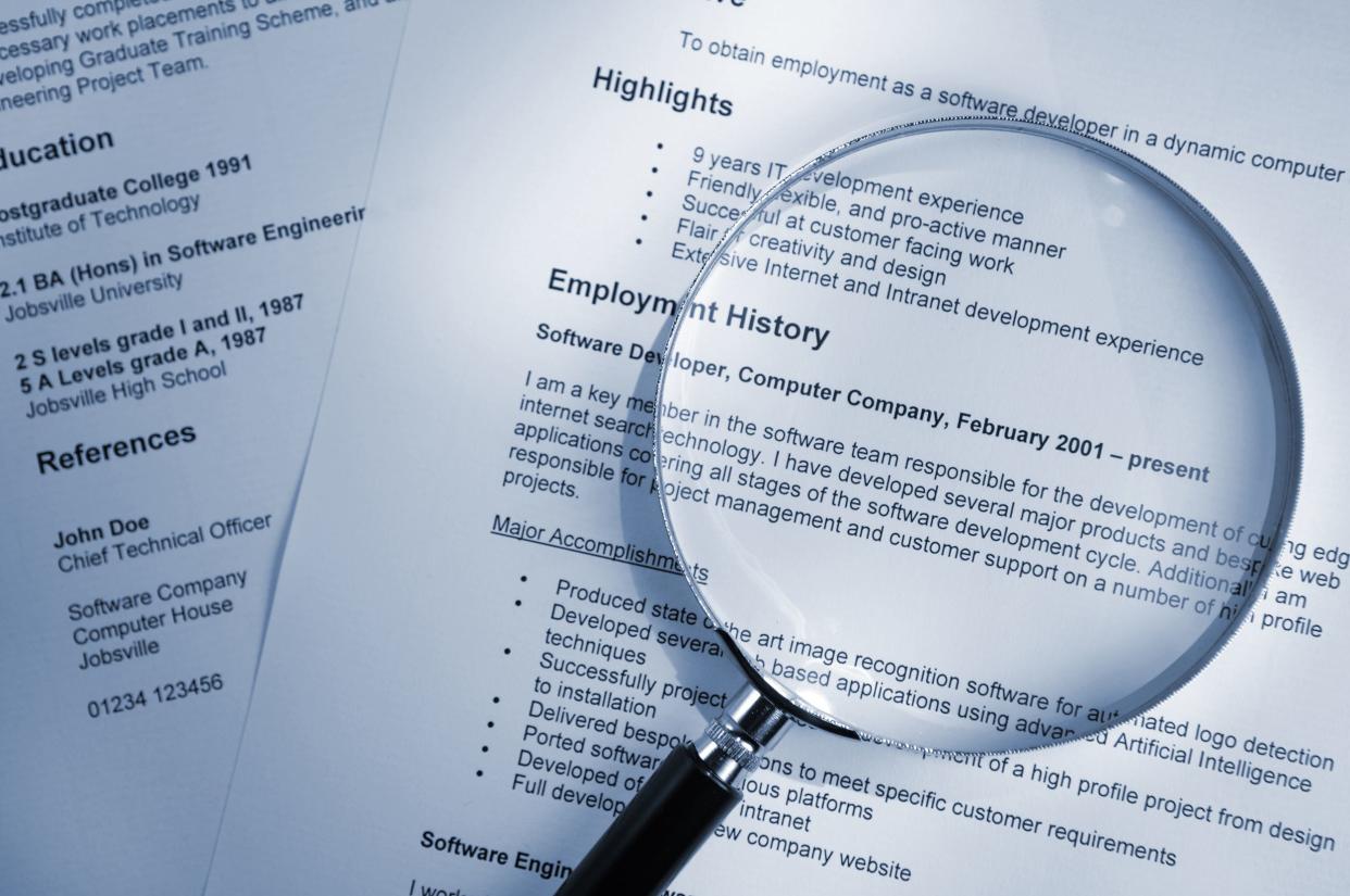 blue tinted image of a magnifying glass lying on top of several sheets of a printout of resume documents