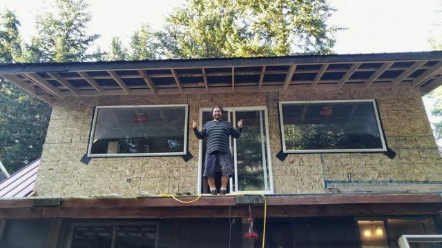 Spi7uew-Sqalemc, the husband of Honey Williams August, is seen in a family photo standing on the roof of the house in Squilax, B.C., that the couple has been building for more than a decade. They lost their home, near Little Shuswap Lake, to the 2023 summer wildfires.