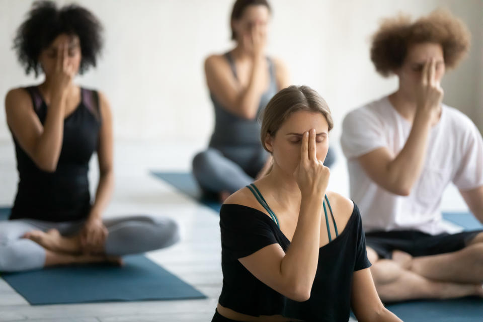 Group of multi ethnic people sitting cross-legged on floor doing yoga practice Alternate Nostril Breathing, exercise reduces stress anxiety, calms rejuvenates nervous system, helps to balance hormones