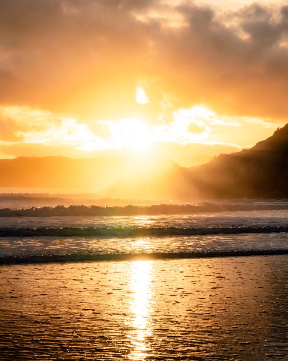 Photo of the beach at sunset with gentle waves all bathed in a golden glow.