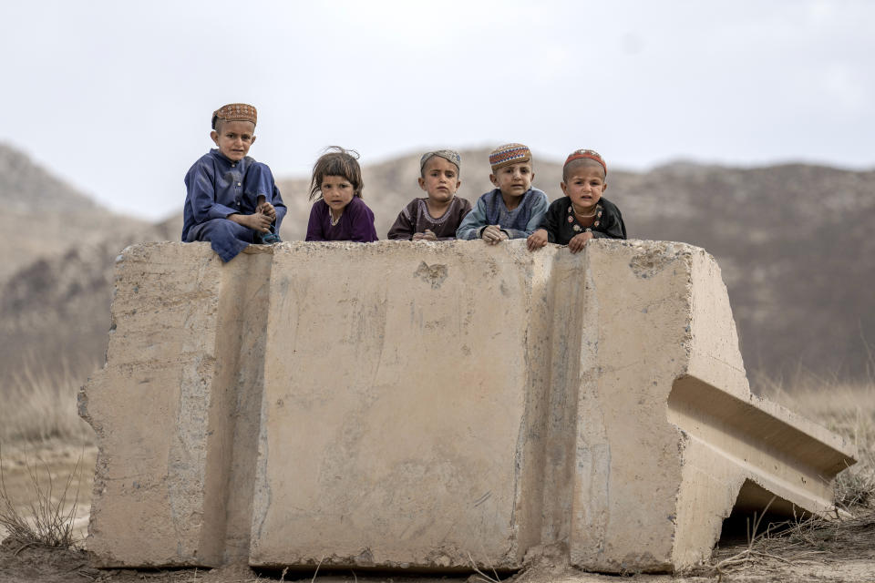 Children sit on a toppled cement barrier on the side of a road to watch passing cars in a village in a remote region of Afghanistan, on Sunday, Feb. 26, 2023. (AP Photo/Ebrahim Noroozi)