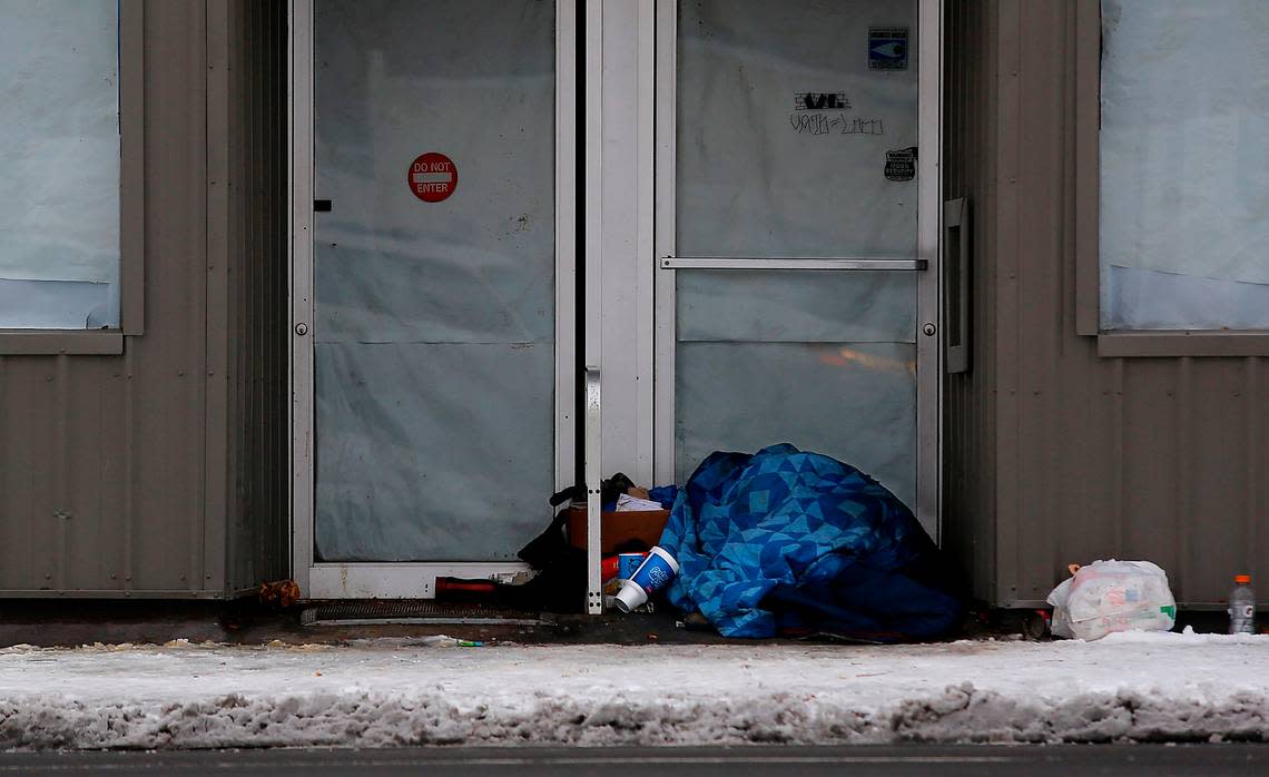 A man sleeps under a blanket with his belongings in the doorway of a closed downtown Kennewick business in December 2022