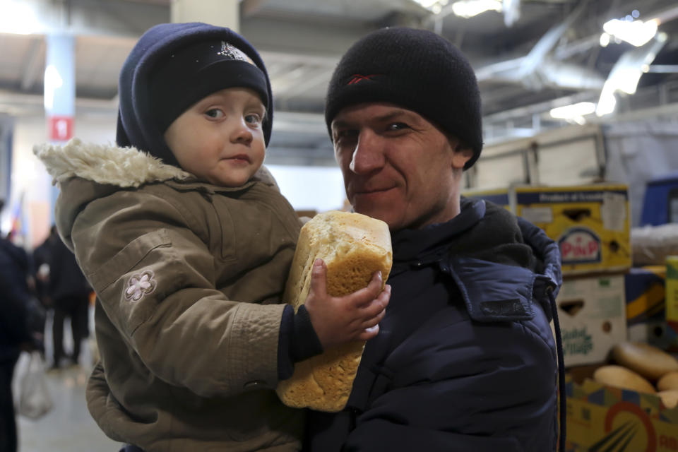 A man and his child look at a photographer as they wait to get a food and drinking water at a supermarket on the territory which is under the Government of the Donetsk People's Republic control, on the outskirts of Mariupol, Ukraine, Thursday, March 24, 2022. (AP Photo/Alexei Alexandrov)