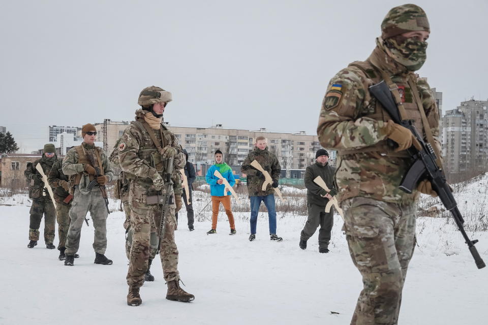 Veterans of the Ukrainian National Guard Azov battalion, some not in uniform, but all holding rifles, conduct military exercises in a snowy landscape.