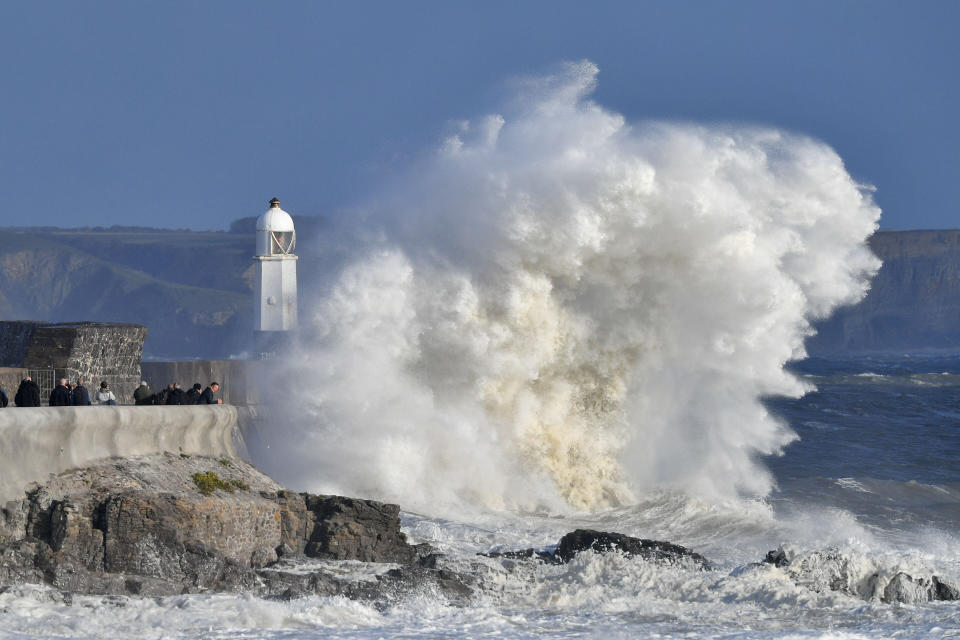 People gather to watch huge waves crash against the harbour wall at Porthcawl, Wales.