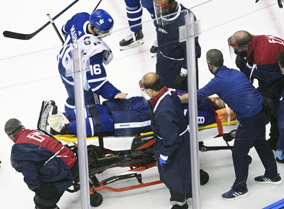 Toronto Maple Leafs defenseman Jake Muzzin (8) leaves the ice on a stretcher as teammate Maple Leafs right wing Mitchell Marner (16) pats him on the pants while playing against the Columbus Blue Jackets during the third period of an NHL hockey playoff game Tuesday, Aug. 4, 2020 in Toronto. (Nathan Denette/The Canadian Press via AP)