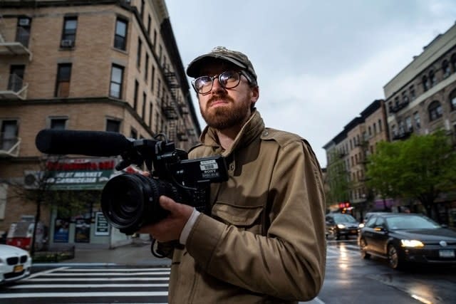 John standing on a street corner holding a large camera