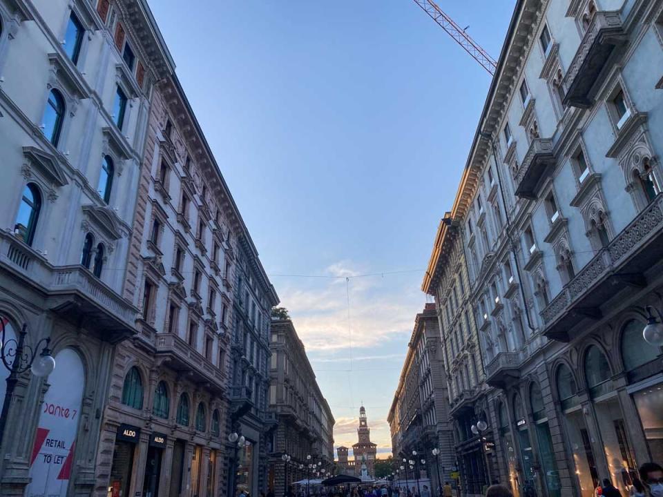 A view of a street and buildings in Milan at sunset.