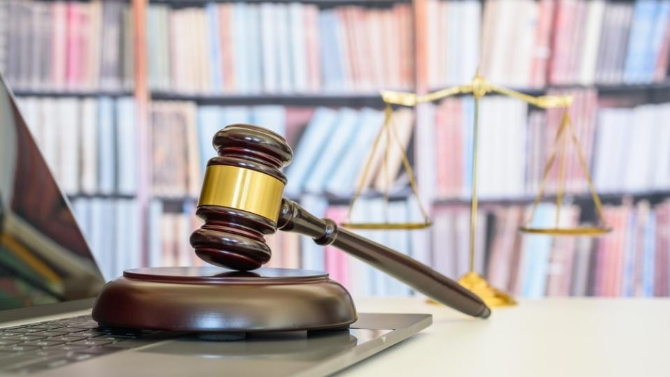 A gavel and scales on a desk with a library in the background.