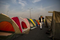 A farmer speaks on his mobile as he walks past tents put up in the middle of a major highway which is blocked in a protest against new farm laws at the Delhi-Uttar Pradesh state border, India, Wednesday, Jan. 20, 2021. Farmers have been blockading highways connecting New Delhi to northern India for nearly seven weeks against new farm laws, obstructing transportation and dealing a blow to manufacturing and businesses in the north. Farmers fear the government will stop buying grain at minimum guaranteed prices and that corporations will then push prices down under the new laws. (AP Photo/Altaf Qadri)