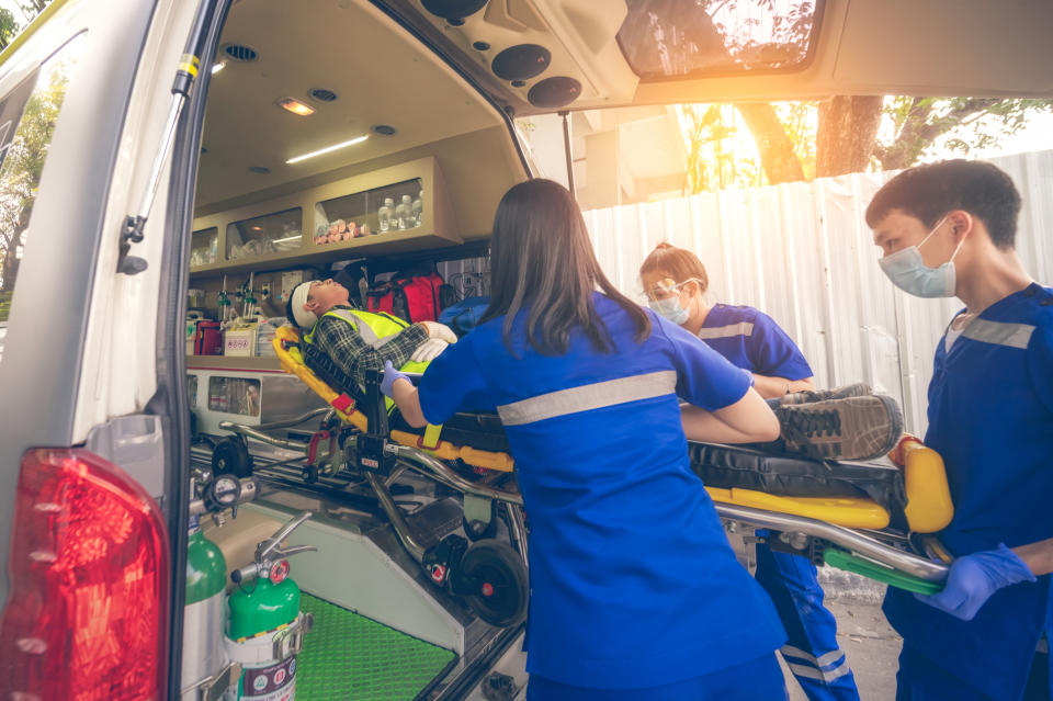 Paramedics assist a person on a stretcher into an ambulance. The person appears to be receiving medical attention