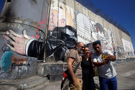 REFILE - ADDING RESTRICTIONS Tourists stand in front of a grafitti depicting U.S President Donald Trump on the controversial Israeli barrier in the West Bank town of Bethlehem August 4, 2017. REUTERS/Mussa Qawasma