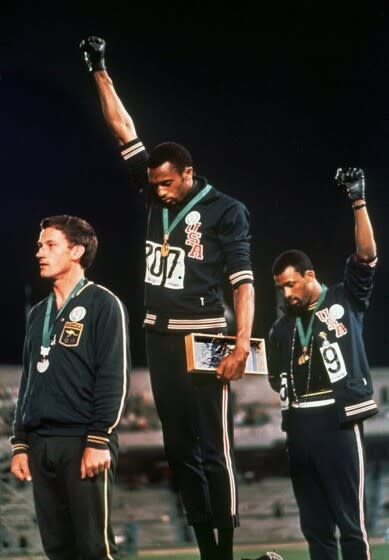 U.S. athletes Tommie Smith, center, and John Carlos stare downward while extending gloved hands skyward in 1968