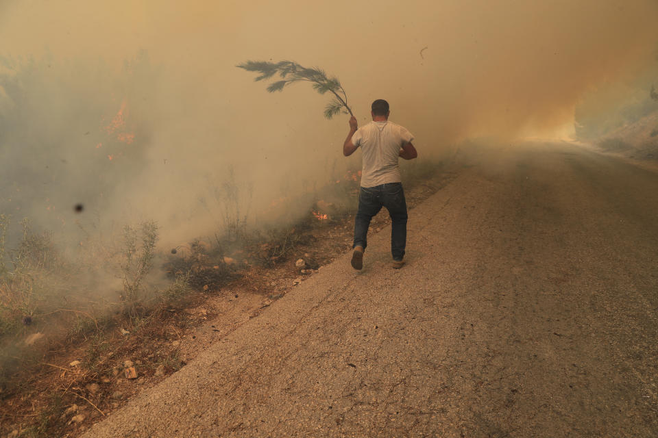 A man runs to extinguish a forest fire, at Qobayat village, in the northern Akkar province, Lebanon, Thursday, July 29, 2021. Lebanese firefighters are struggling for the second day to contain wildfires in the country's north that have spread across the border into Syria, civil defense officials in both countries said Thursday. (AP Photo/Hussein Malla)