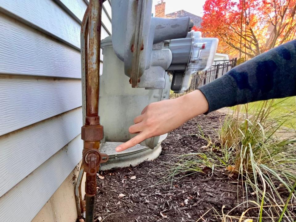 Woman pointing to shut off valve on home's exterior gas line. 