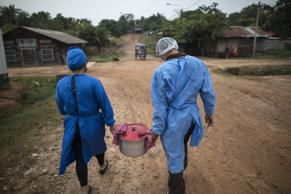 Mery Fasabi (izquierda) y Isai Eliaquin Sanancino cargan con una olla de hierbas remojadas en agua hirviendo a la casa de una mujer infectada de coronavirus, en la comunidad indígena Shipibo de Pucallpa, en la región peruana de Ucayali, el 1 de septiembre de 2020. Fasabi, junto a otros 15 voluntarios levantó un centro de tratamiento improvisado conocido por los locales como Comando Matico, que trata el coronavirus con un enfoque holístico. (AP Foto/Rodrigo Abd)