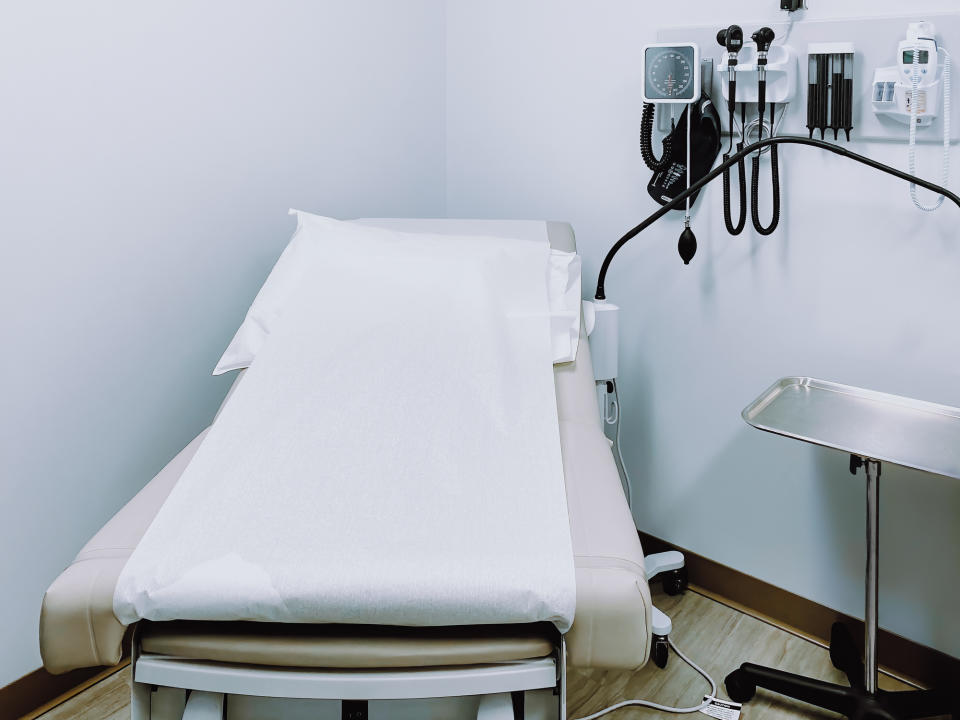 Empty doctor's examination room with a paper-covered exam table and medical equipment on the wall