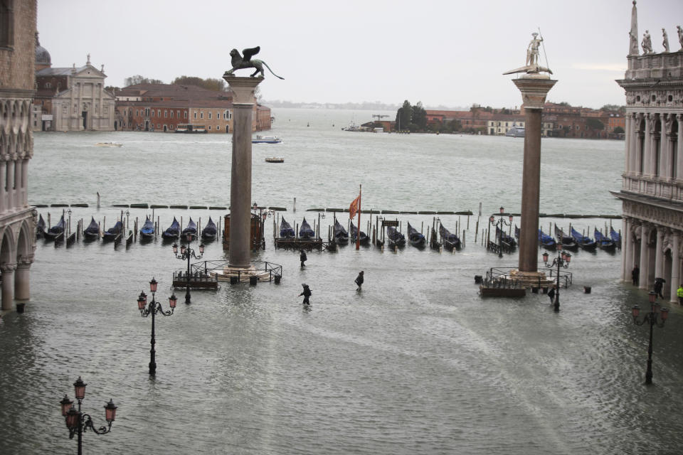 People make their way in a flooded St. Mark's Square in Venice, Italy, Friday, Nov. 15, 2019. Waters are rising in Venice where the tide is reaching exceptional levels just three days after the Italian lagoon city experienced its worst flooding in more than 50 years. (AP Photo/Luca Bruno)