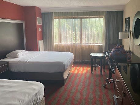 A hotel room with two beds, a window, and a desk.