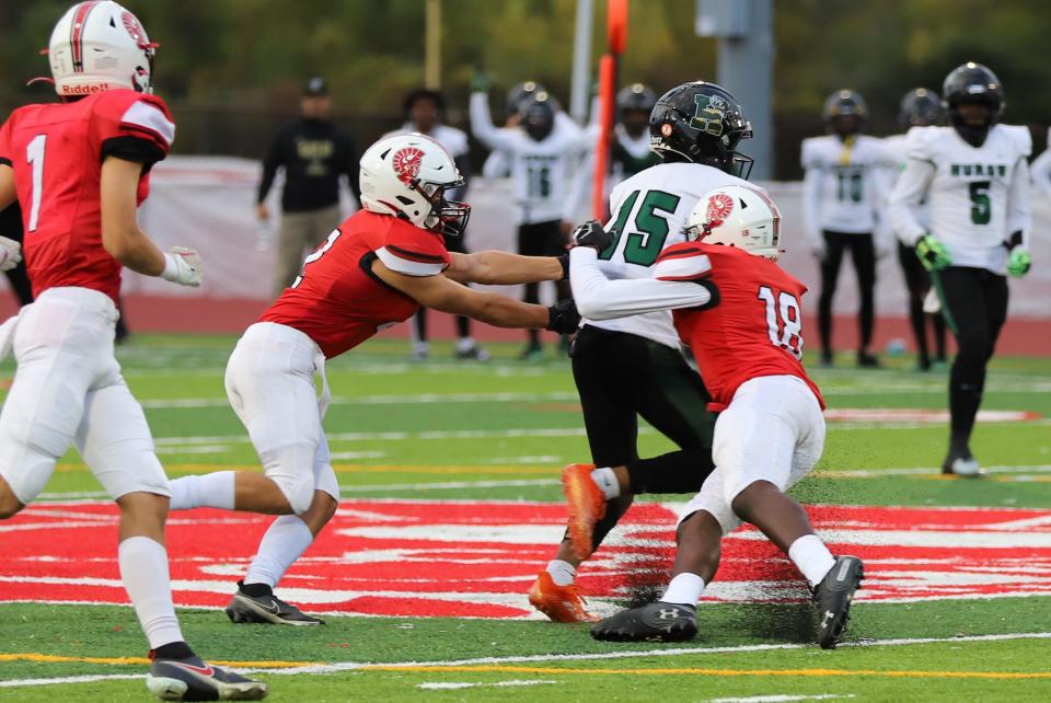 Michael Burns (right) and Logan Loveland bring down Ladanian Woods of Ann Arbor Huron Friday night.