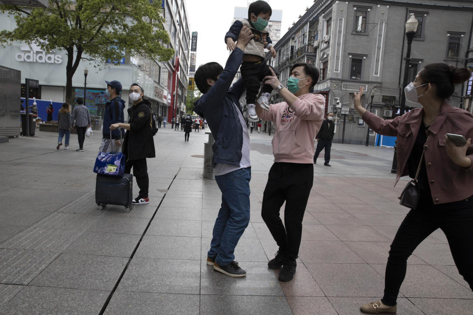 In this Wednesday, April 8, 2020, photo, a child is lifted in the air as residents visit a retail street in Wuhan in central China's Hubei province. Released from their apartments after a 2 1/2-month quarantine, residents of the city where the coronavirus pandemic began are cautiously returning to shopping and strolling in the street but say they still go out little and keep children home while they wait for schools to reopen. (AP Photo/Ng Han Guan)