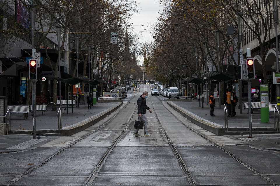 A man wearing a face mask walks across a road in Melbourne.