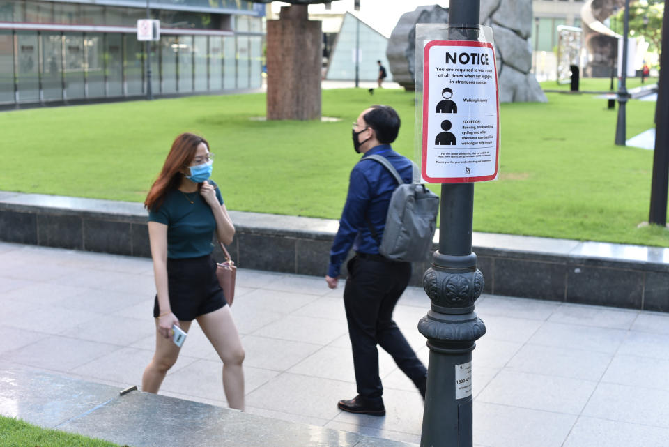 A notice reminding people to wear masks hangs on a post as people walk by in Singapore Tuesday, June 2, 2020. Singapore reopened 75 percent of its economy Tuesday, as part of a three-phase controlled approach to end a virus lockdown since early April. (AP Photo/YK Chan)