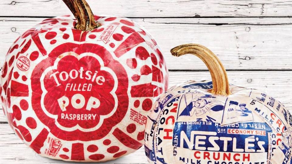 two pumpkins each decoupaged with vintage candy wrappers, including nestles crunch bars and a giant tootsie pop