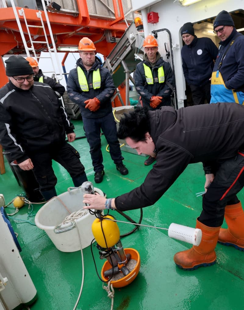 On board the fisheries research vessel Solea on the Baltic Sea, Thomas Noack, biologist and fisheries technician at the Thünen Institute of Baltic Sea Fisheries, prepares a sensor camera with bait for use, crew members and fishermen look on. Bernd Wüstneck/dpa