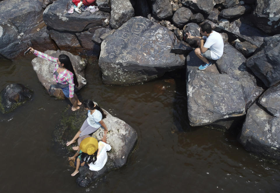 Residents take selfies of rock paintings at the Ponta das Lajes archaeological site, in the rural area of Manaus, Brazil, Saturday, Oct. 28, 2023. The archaeological site was exposed following a drought in the Negro River, unveiling rock paintings that, according to archaeologists, date back between 1,000 and 2,000 years. (AP Photo/Edmar Barros)
