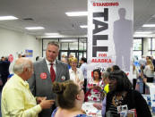 Republican gubernatorial candidate Mike Dunleavy, second from left, stands near his campaign table at a meet-and-greet event and a sign bearing a slogan that riffs on his height, in the lobby of Anchorage Baptist Temple, Sunday, Aug. 19, 2018, in Anchorage, Alaska. The event, in which candidates have tables and parishioners can meet them and ask questions, has become a tradition for the church in the lead-up to elections. (AP Photo/Becky Bohrer)