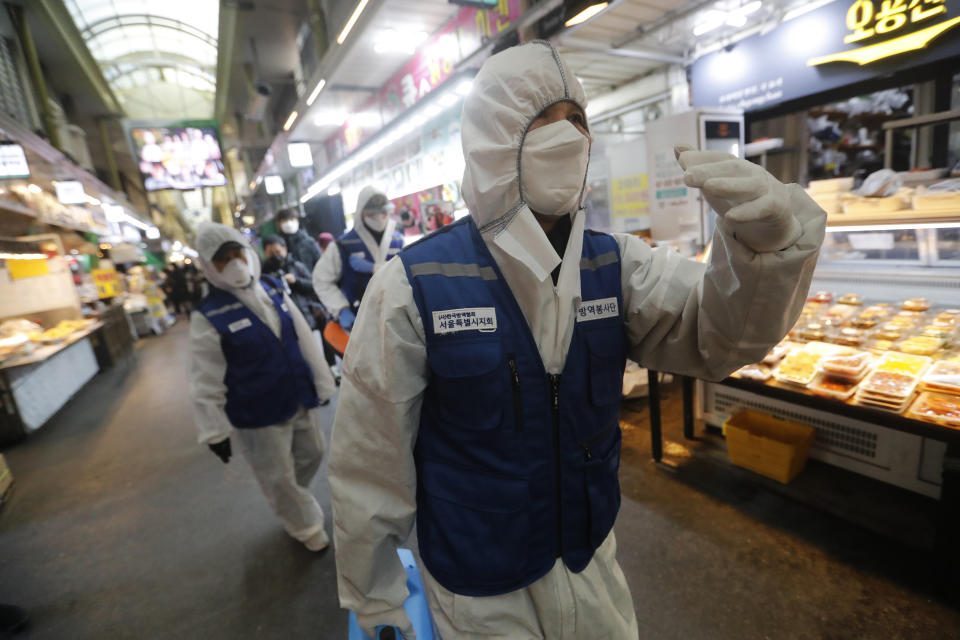 Trabajadores con equipo de protección llegan para rocíar desinfectante como precaución contra el coronavirus en un mercado en Seúl, Corea del Sur, el lunes 24 de febrero de 2020. (AP Foto/Ahn Young-joon)