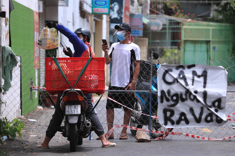 A delivery man hands over food order to another at a fence set up block traffic in Vung Tau, Vietnam, Monday, Sept. 13, 2021. The sign at right reads "No non-resident". The roadblocks and barricades make the streets of this southern Vietnamese city look like they did during the war that ended almost 50 years ago. But this time, the battle is being fought against the rampaging coronavirus.(AP Photo/Hau Dinh)