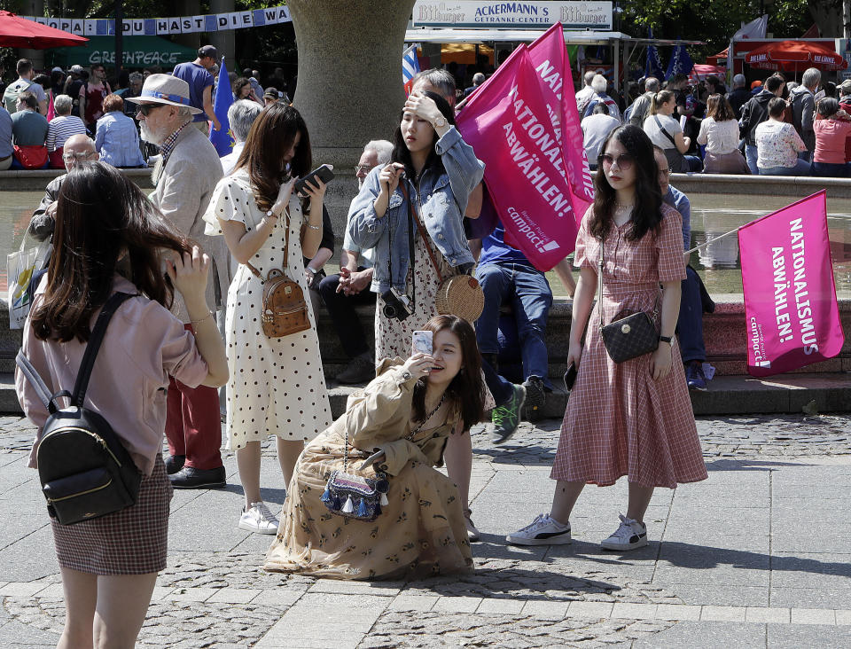 Chinese tourists take photographs and selfies in front of the Old Opera during a demonstration in Frankfurt, Germany, Sunday, May 19, 2019. People across Europe attend demonstrations under the slogan 'A Europe for All - Your Voice Against Nationalism'. Pink banners reads 'Deselect Nationalism'. (AP Photo/Michael Probst)