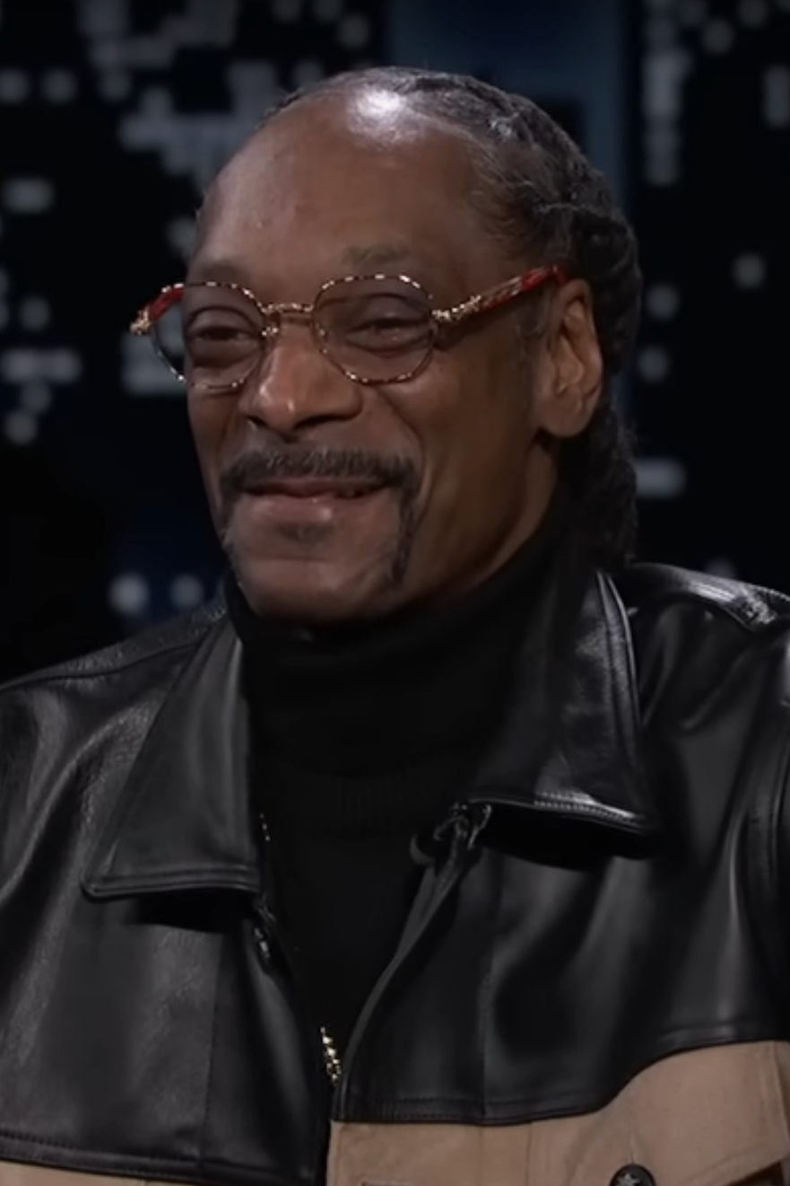 Snoop Dogg smiling, wearing tinted glasses and a black leather jacket