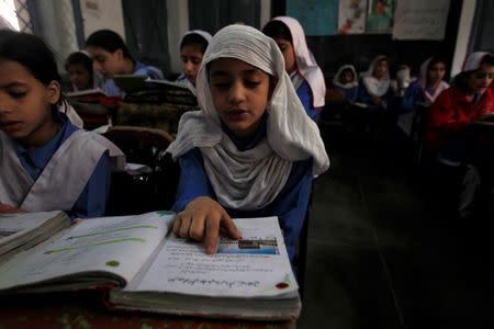 A girl reads a book while attending her daily class with others at a government school in Peshawar October 29, 2014. REUTERS/Fayaz Aziz