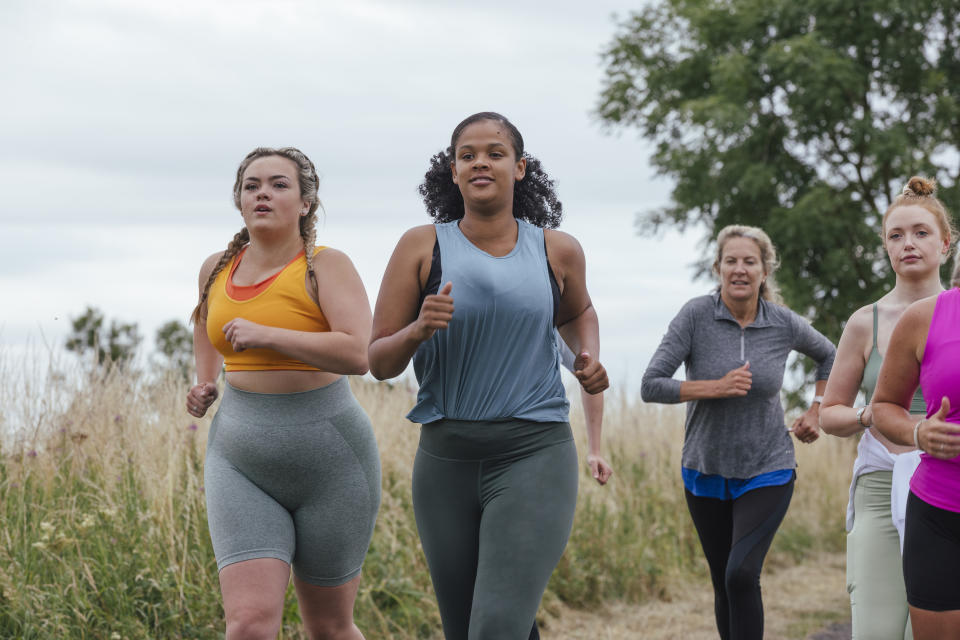 A front-view shot of a group of female friends running outdoors by a field in Northumberland, England.