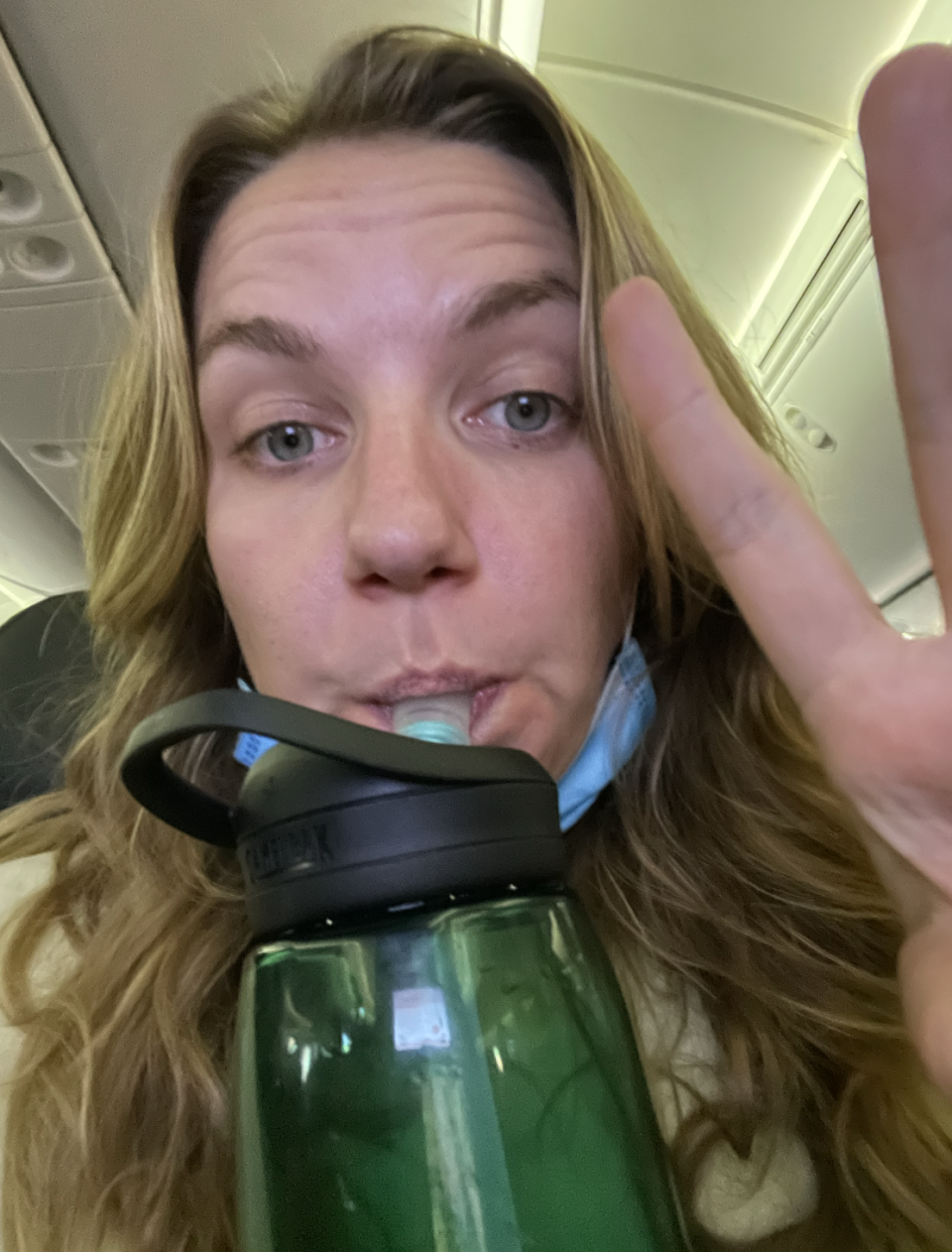 A selfie of a girl sitting in a plane seat, she's sipping from a water bottle