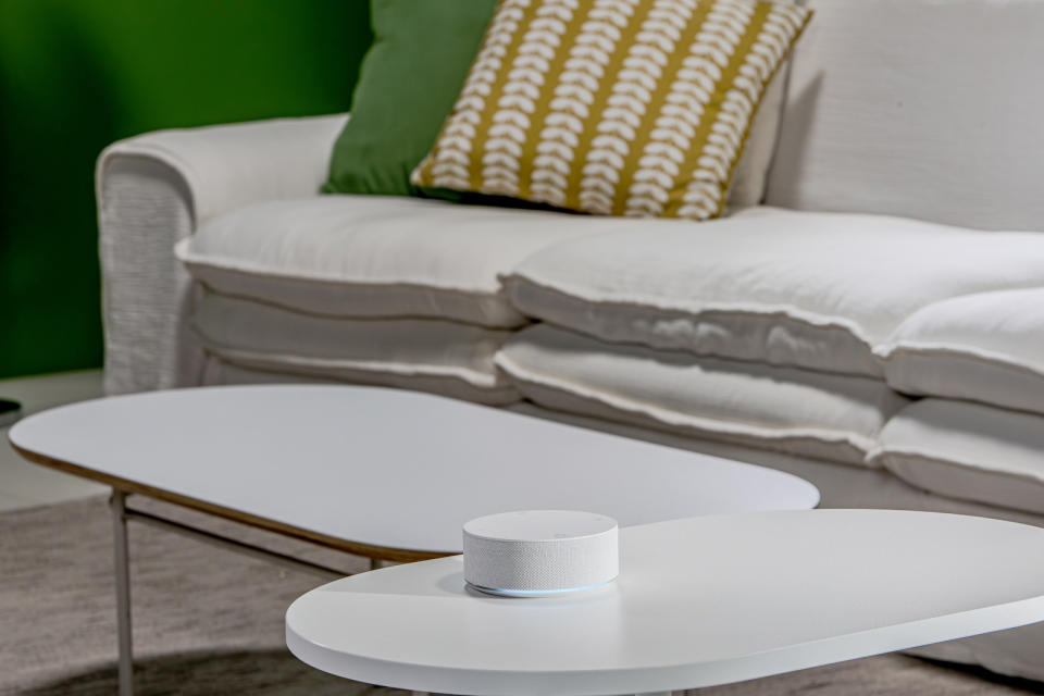 A small white puck-like device on a white table with a couch in the background.