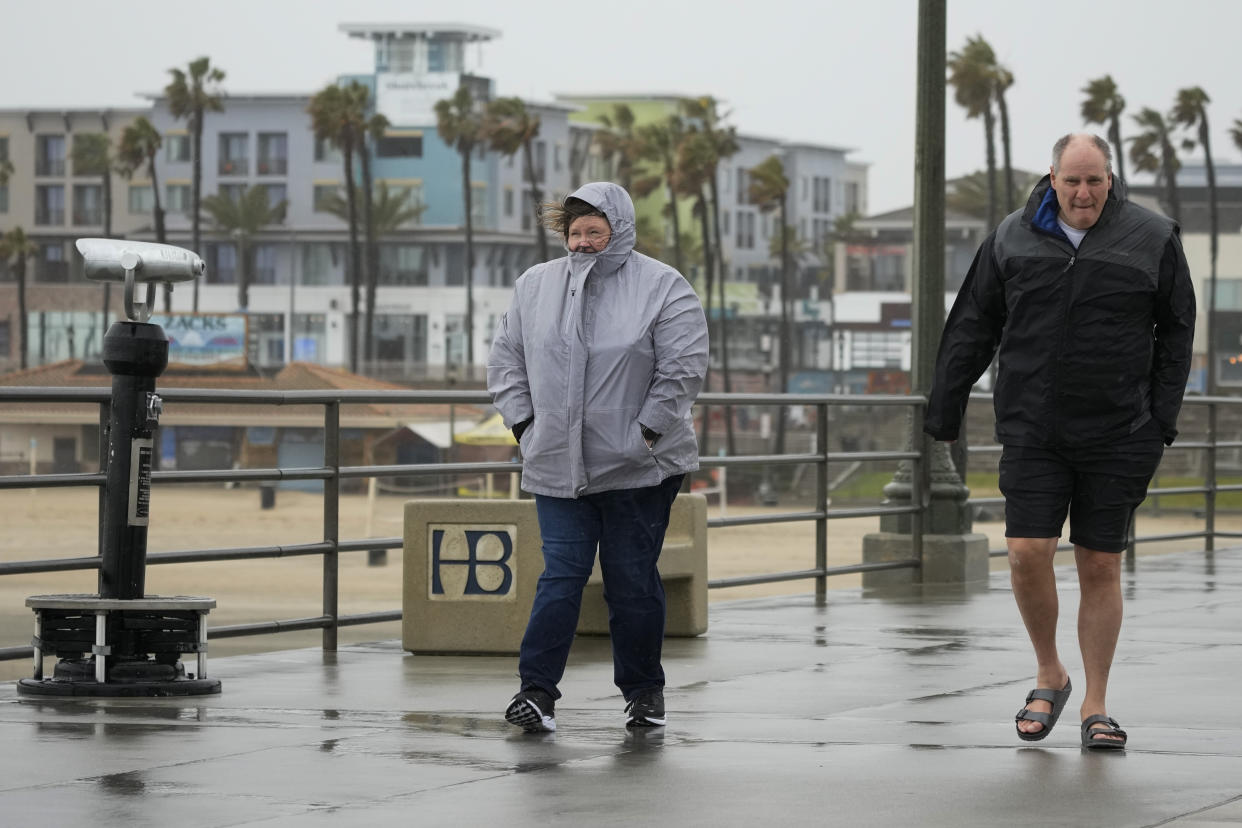 People walk along the Huntington Beach Pier on Friday, Feb. 24, 2023, in Huntington Beach, Calif. California and other parts of the West faced heavy snow and rain Friday from the latest winter storm to pound the U.S. (AP Photo/Ashley Landis)