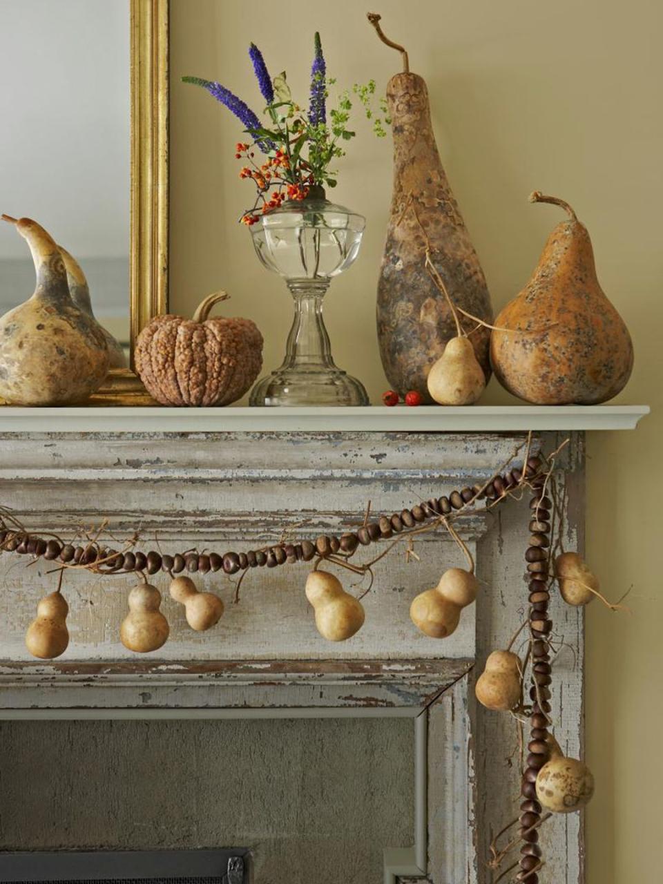 <p>Dried gourds and squash form a still life on this rustic mantel. Additional 'Tiny Bottle' gourds hang from a garland of farm stand chestnuts.</p>