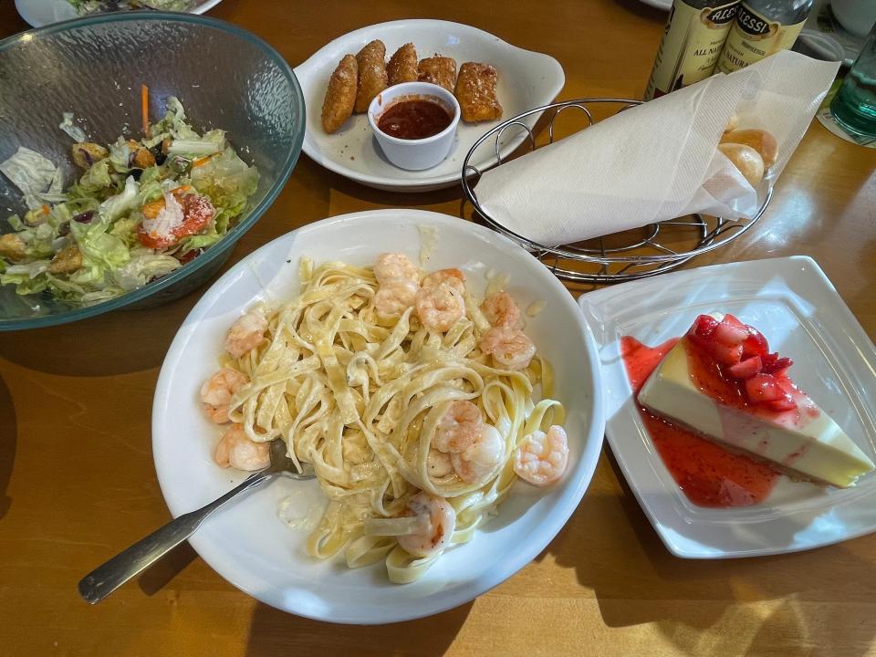 Table full of shrimp Alfredo, strawberry cheesecake, mozzarella sticks, breadsticks, and salad at Olive Garden