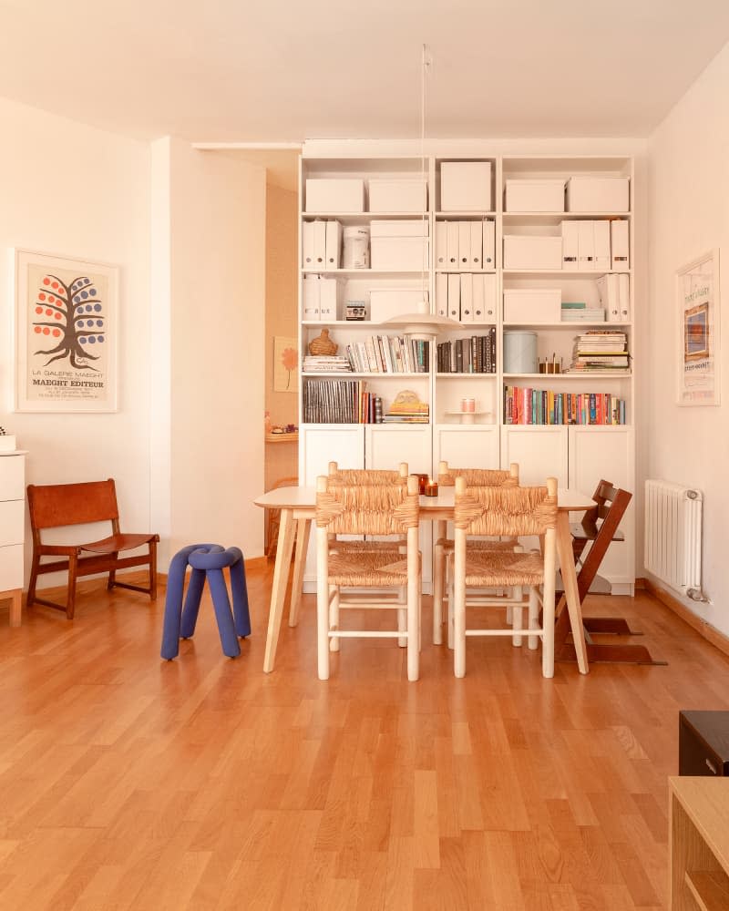 white dining room with tall bookshelves and light wood table, light wood and rattan dining chairs