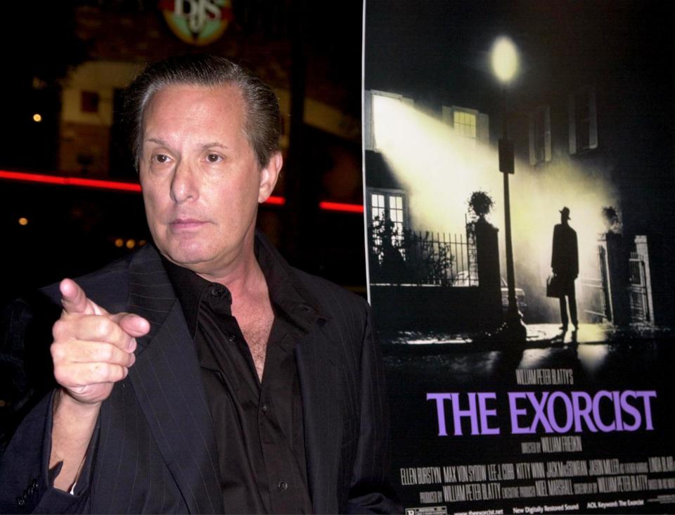 William Friedkin in a black suit next to a poster of The Exorcist