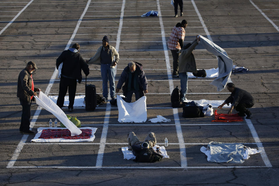People prepare places to sleep in area marked by painted boxes on the ground of a parking lot at a makeshift camp for the homeless Monday, March 30, 2020, in Las Vegas. Officials opened part of a parking lot as a makeshift homeless shelter after a local shelter closed when a man staying there tested positive for the coronavirus. (AP Photo/John Locher)