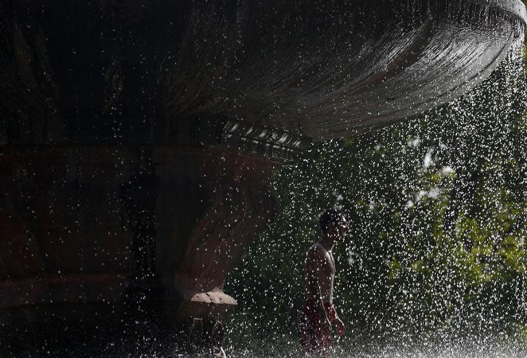 An Indian youth stands under a fountain near India Gate amid soaring temperatures in New Delhi, on May 27, 2015